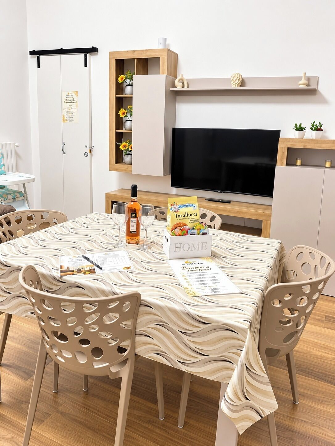 Zona pranzo con tavolo apparecchiato per quattro, televisione e mobile contenitore con oggetti decorativi.