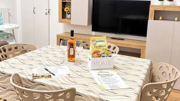 Zona pranzo con tavolo apparecchiato per quattro, televisione e mobile contenitore con oggetti decorativi.
