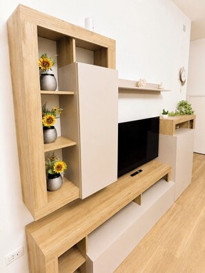 A modern living room with a built-in TV, wooden shelves with decorative vases, and a small plant on a side table. - Sunset Home: A newly renovated vacation rental right in the heart of the city (Bernalda)