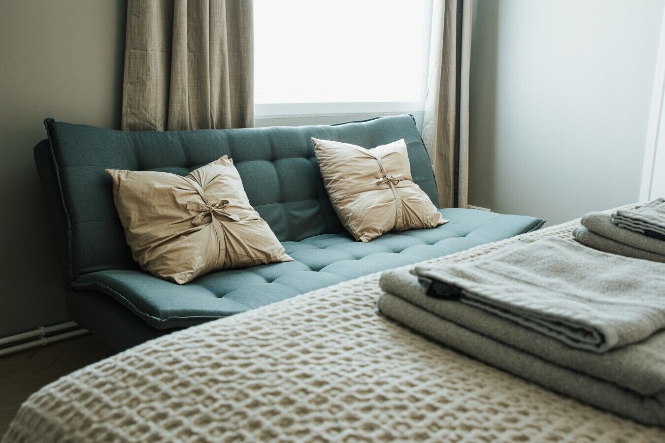 A bed with a textured white cover, a teal upholstered headboard, and two beige pillows tied with a ribbon.
