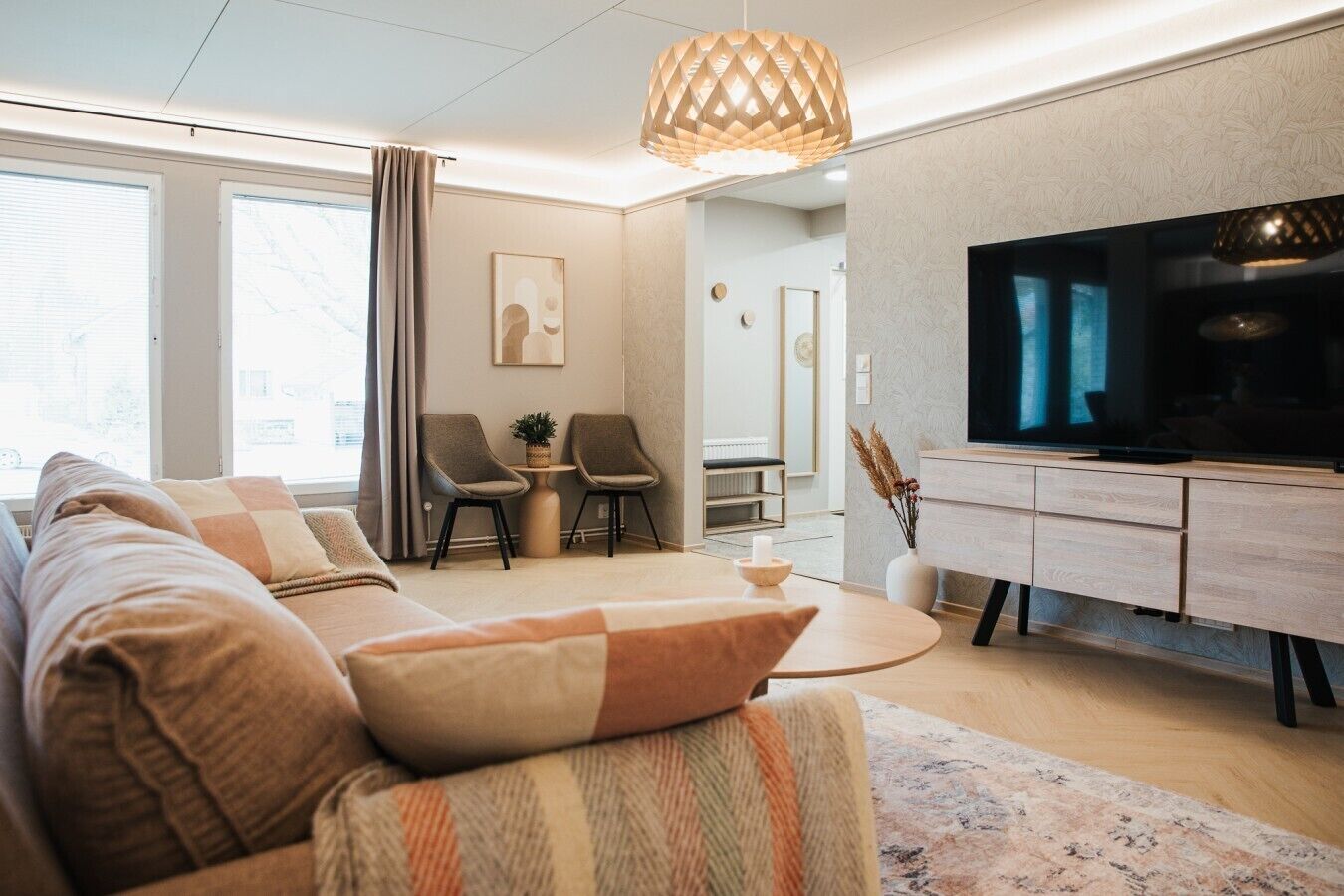 Ein modernes Wohnzimmer mit Sofa, Sesseln, Fernseher und Essbereich.