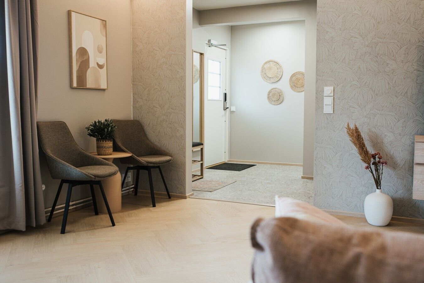 Un salon moderne comprenant un canapé, deux fauteuils, une table basse et un vase décoratif contenant des plantes séchées.