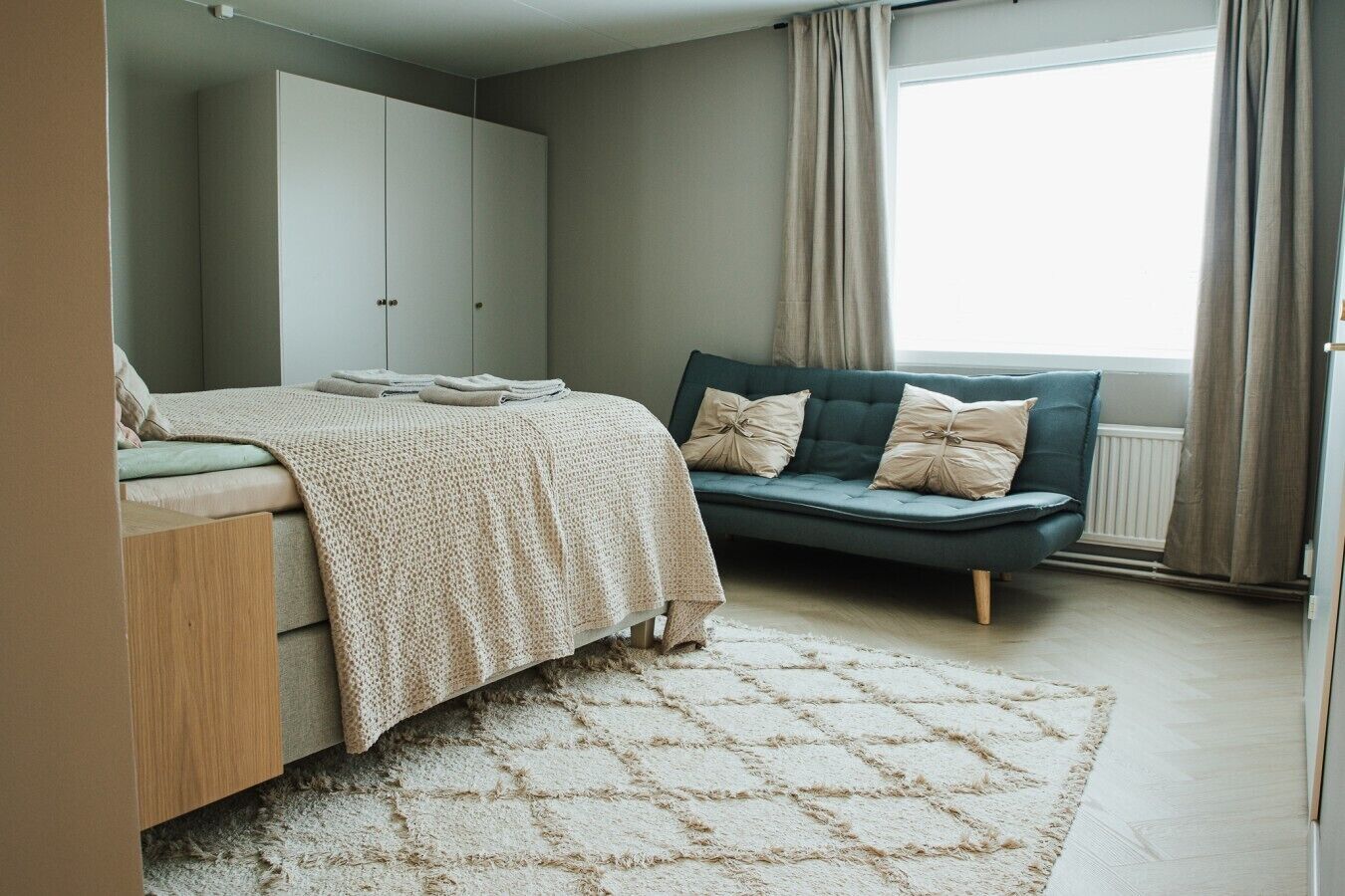 Une chambre à coucher avec un lit, un canapé, une armoire et une fenêtre avec des rideaux.