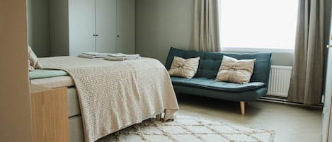 A bedroom with a bed, a sofa, a wardrobe, and a window with curtains.