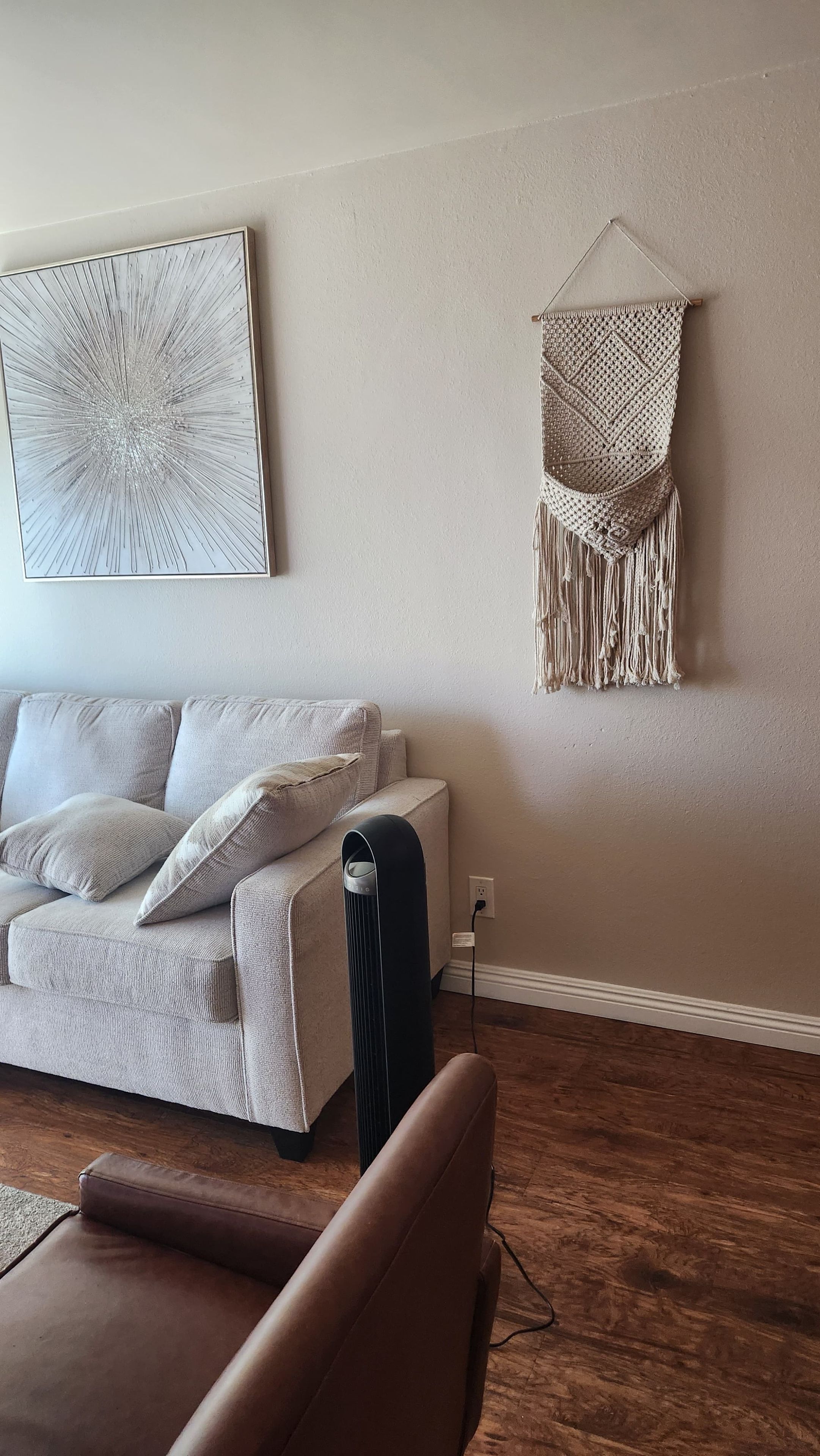 A living room with a sofa, a coffee table, a wall-mounted macrame piece, and a framed abstract artwork.