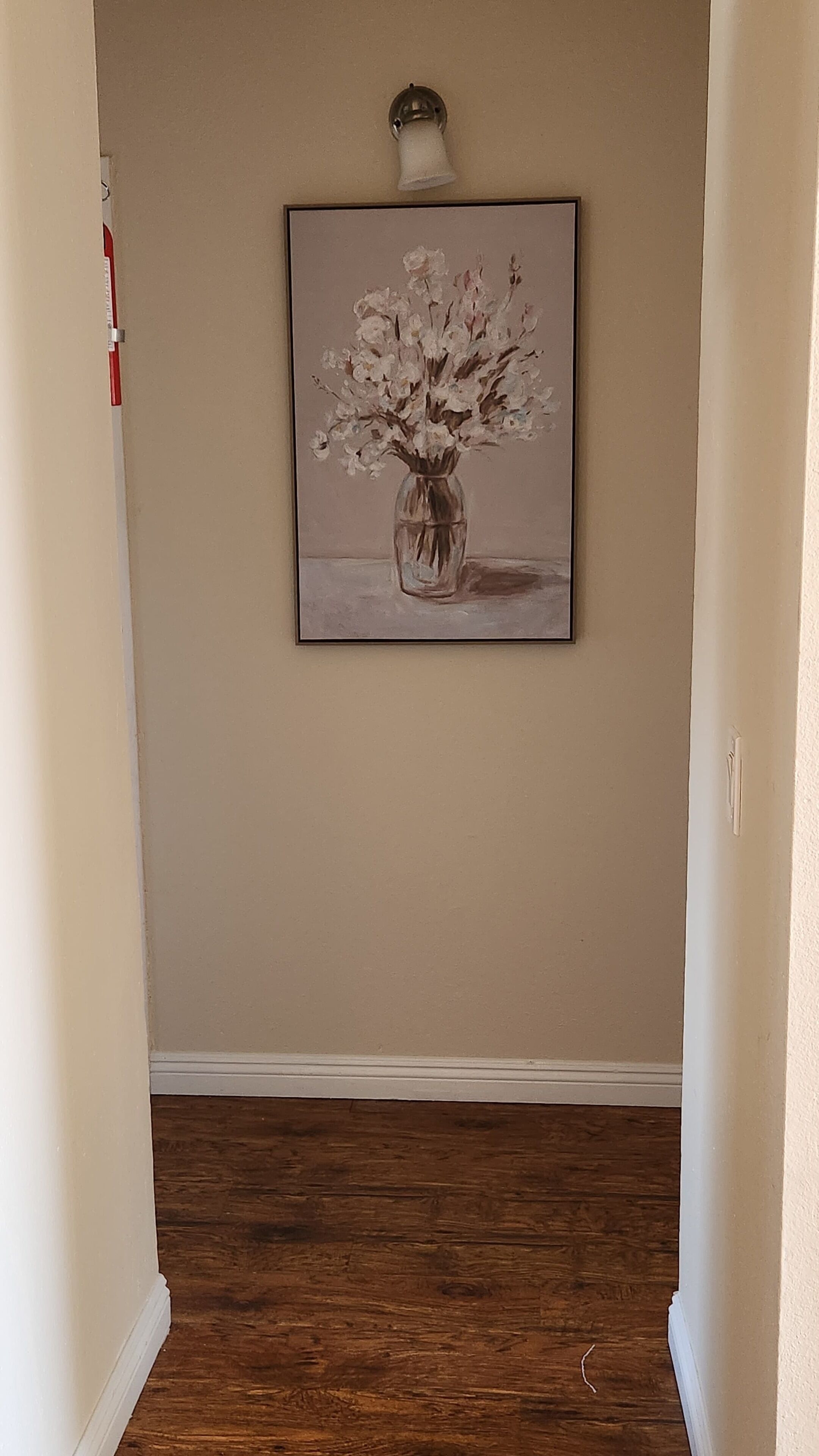 A hallway with a framed artwork of a vase with flowers on the wall.