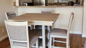 Zona pranzo con tavolo e sedie in legno, ventilatore a soffitto e angolo cottura con mobili ed elettrodomestici.