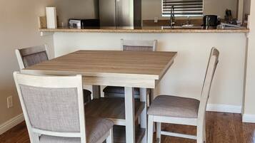 A dining area with a wooden table and chairs, a ceiling fan, and a kitchen area with cabinets and appliances.