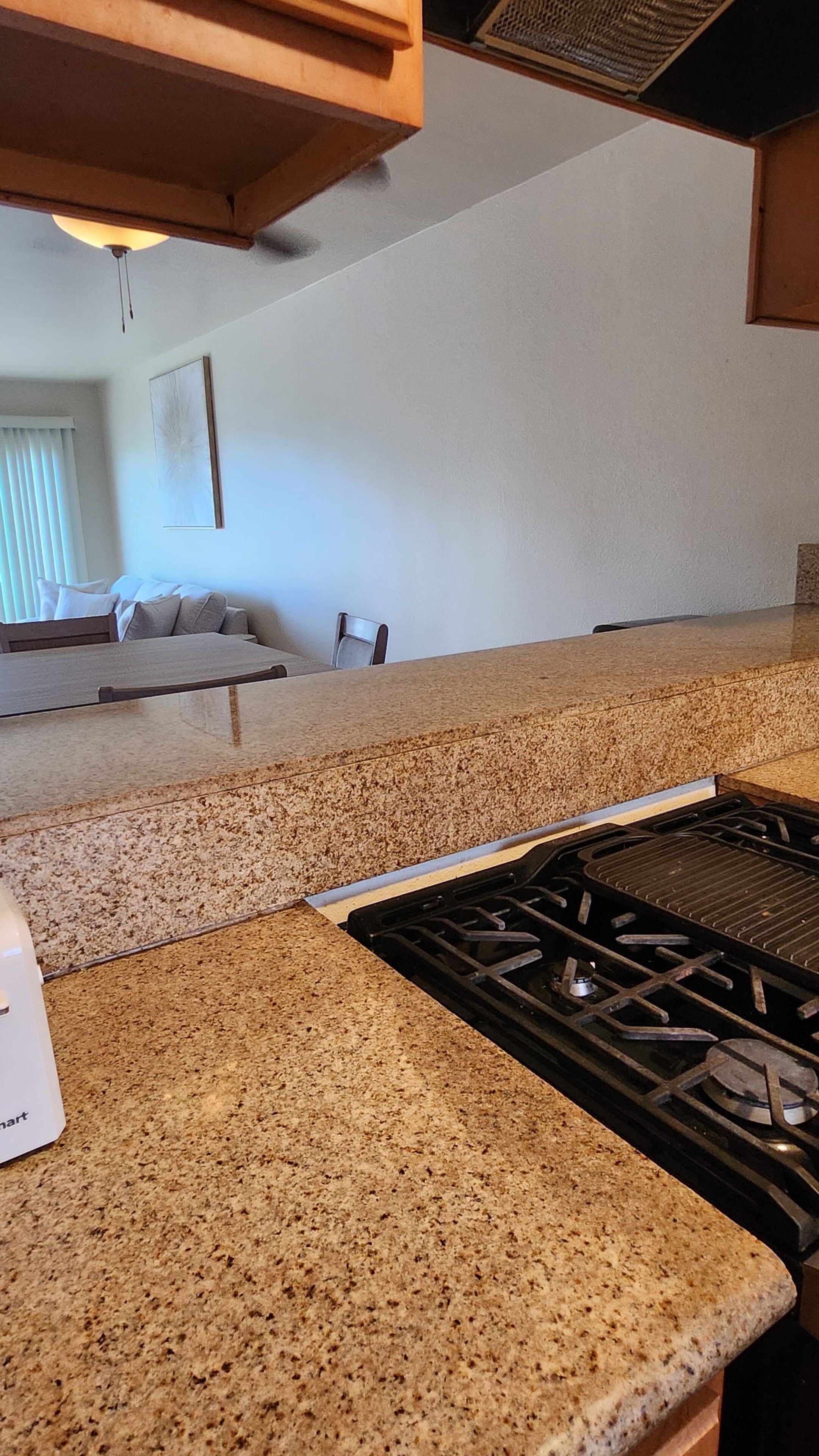 A kitchen with a granite countertop, a stove, and a dining area with a couch and a chair.