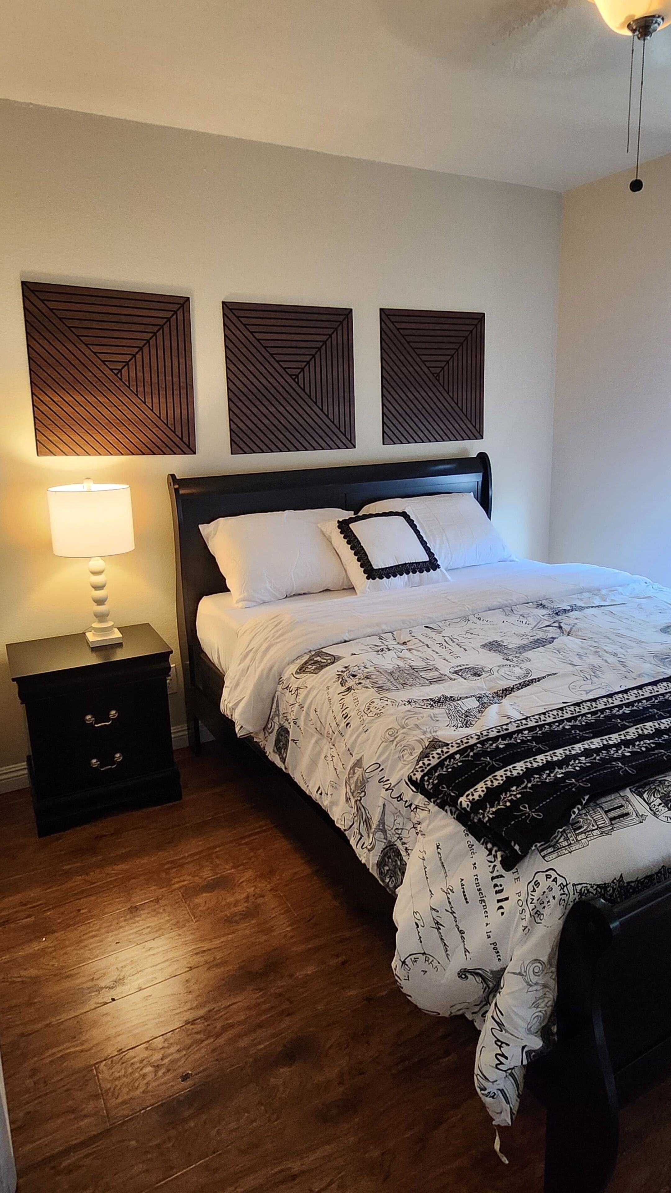 A bedroom with a bed, a nightstand, a lamp, and three wall-mounted decorative panels.