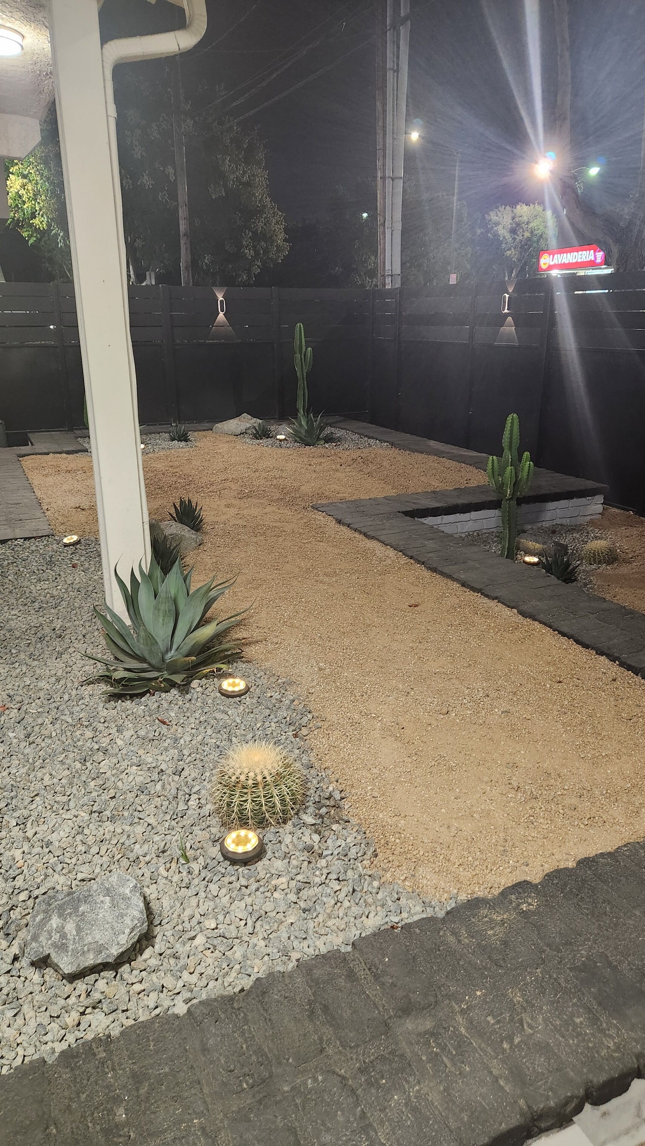 A nighttime outdoor area with a gravel pathway, cacti, and a white pillar.