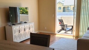 A modern living room with a dining table, a sofa, a TV on a cabinet, and a sliding glass door leading to an outdoor area.