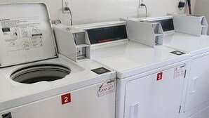 A laundry facility with multiple washing machines and dryers, instructional signs, and a payment terminal.