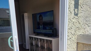 An open sliding door leading to a living area with a television, a cabinet, and a bench.