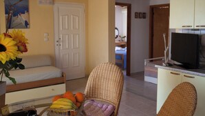 A living room with a sofa, a wicker chair, a television, and a door leading to another room. - Amalia House Garden (Pefki)