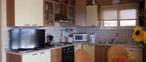 Une cuisine avec des meubles en bois, un four à micro-ondes, une machine à café et un coin repas comprenant une chaise en osier et un panier de fruits.