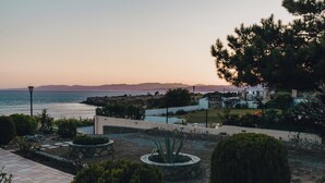 A coastal landscape with a paved walkway, a circular garden, and a view of the sea and distant mountains. - Amalia House Garden (Pefki)
