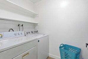 A laundry room with a front-loading washer and dryer, a shelf above the washer, and a blue laundry basket against the wall. - Newly remodeled home 3/2 baths/ free Wi-Fi/ washer/ dryers/ parking in San Jose (San Jose)