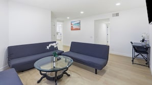 A modern living room with two sofas, a glass coffee table, and a painting on the wall.