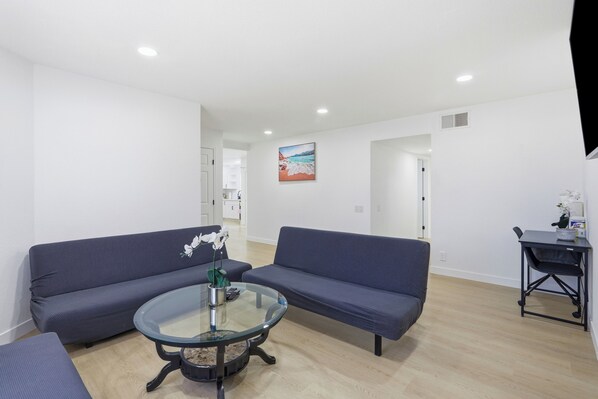 A modern living room with two sofas, a glass coffee table, and a painting on the wall.