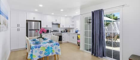 A modern kitchen with white cabinets, a stainless steel refrigerator, and a dining area with a table set for four.