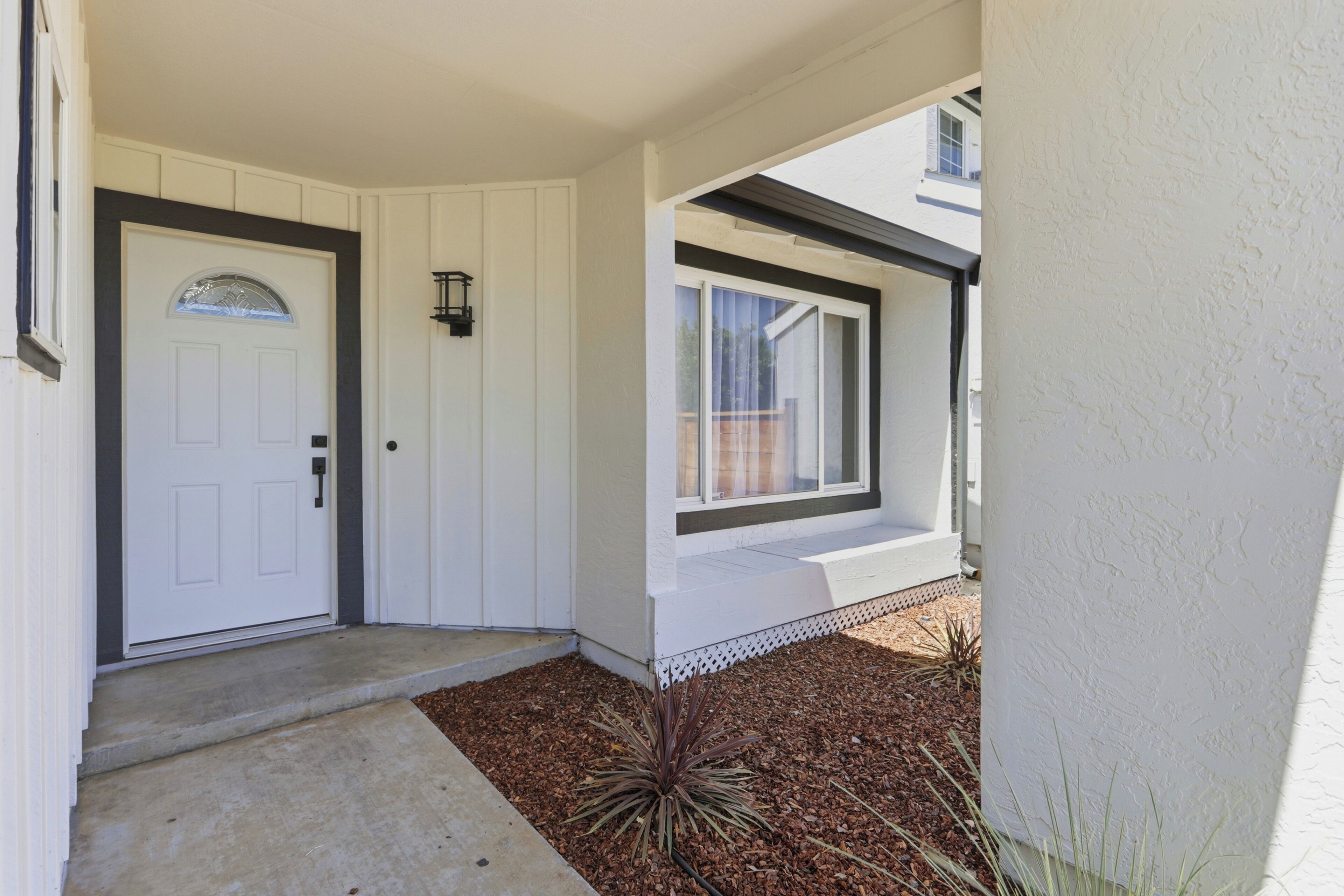 A house entrance with a white door, a small window with a white frame, and a concrete pathway leading to the door.