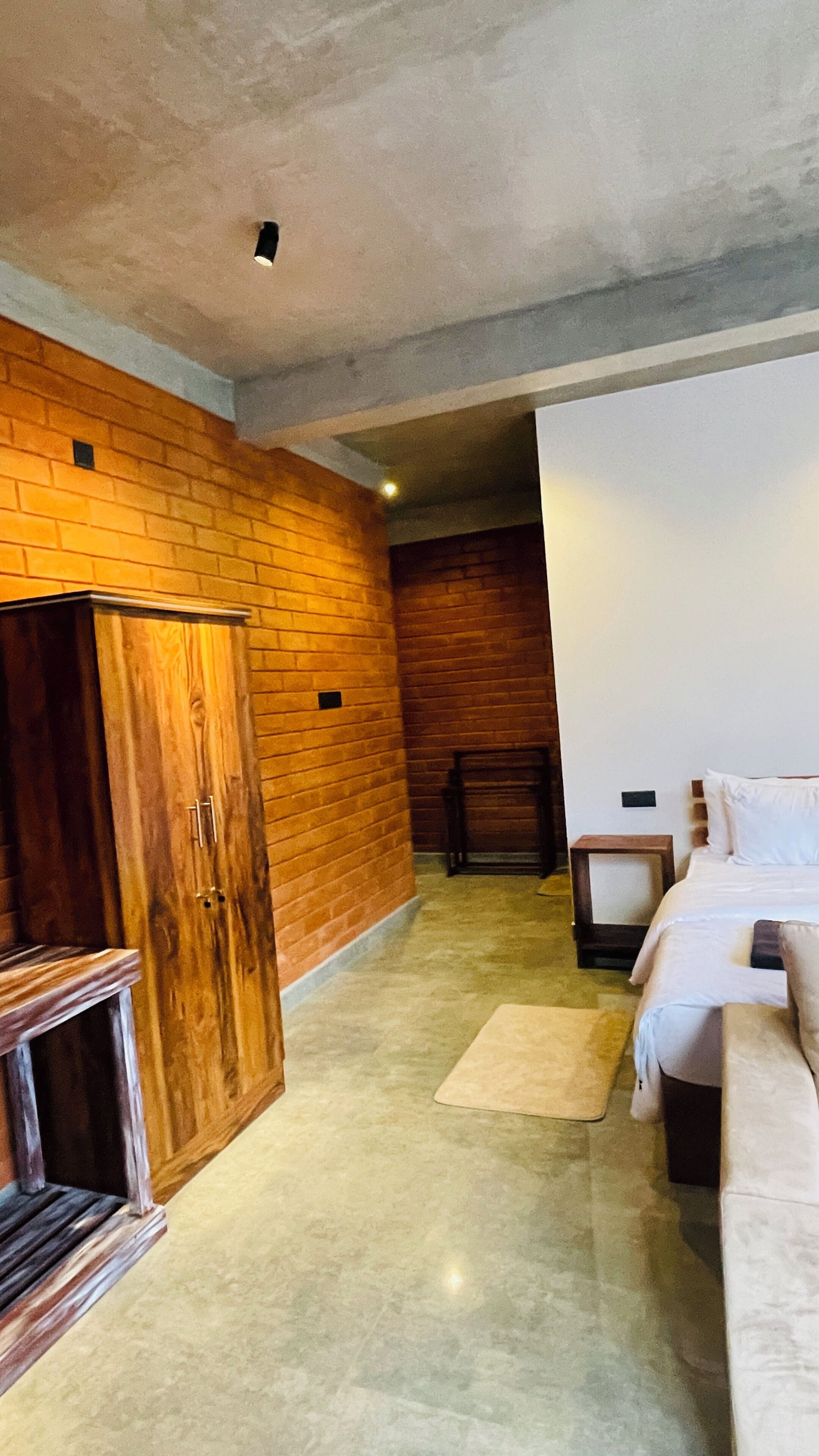 Una habitación con pared de ladrillo, armario de madera, cama y una mesita.