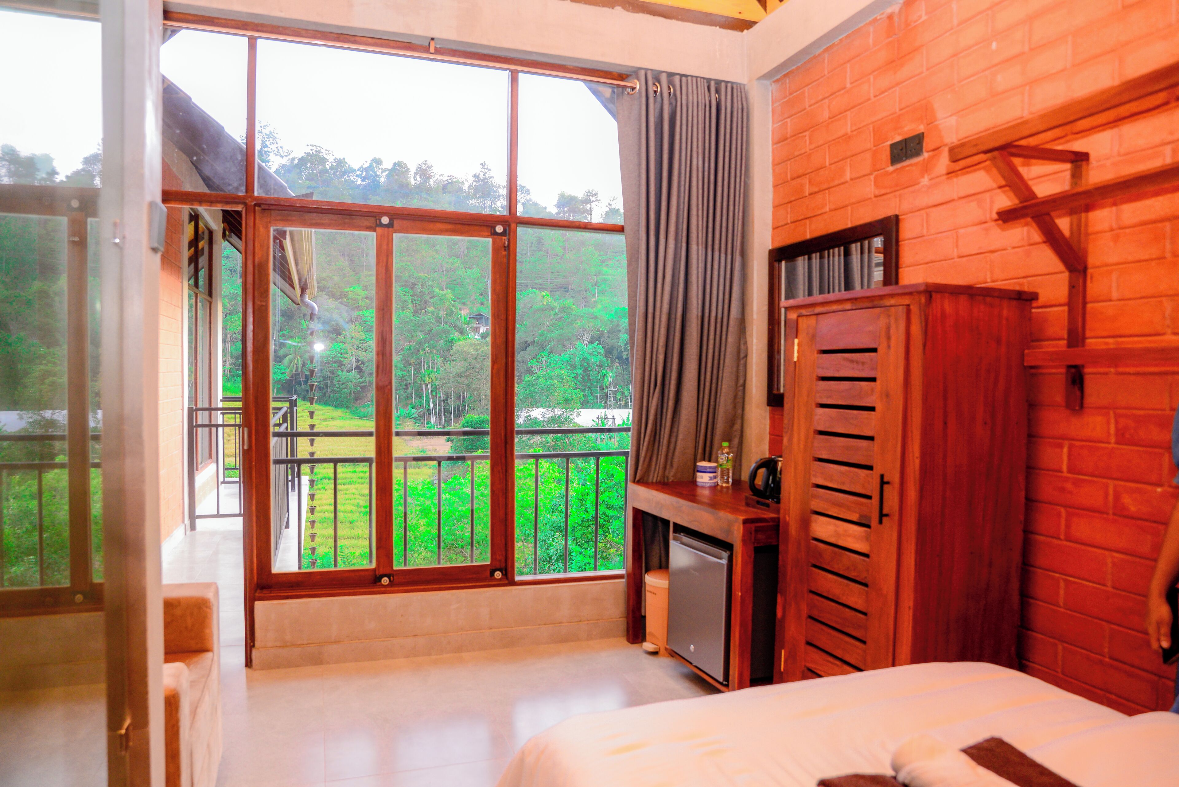 Habitación de hotel con un ventanal grande, una cama, un armario de madera y una pequeña cocina.