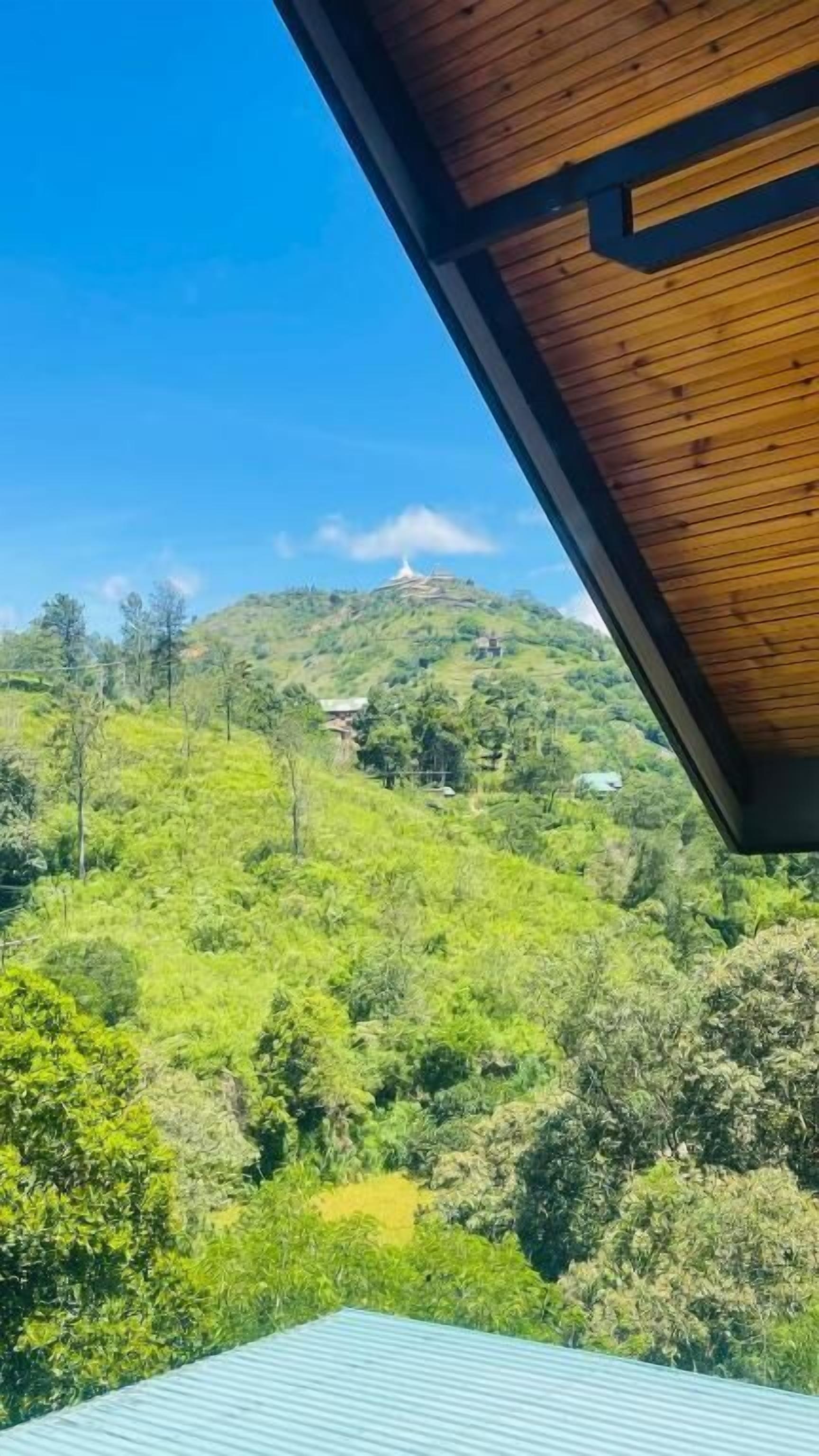 A view from a room with a sloped ceiling, overlooking a lush green landscape with a hill and a structure in the distance.