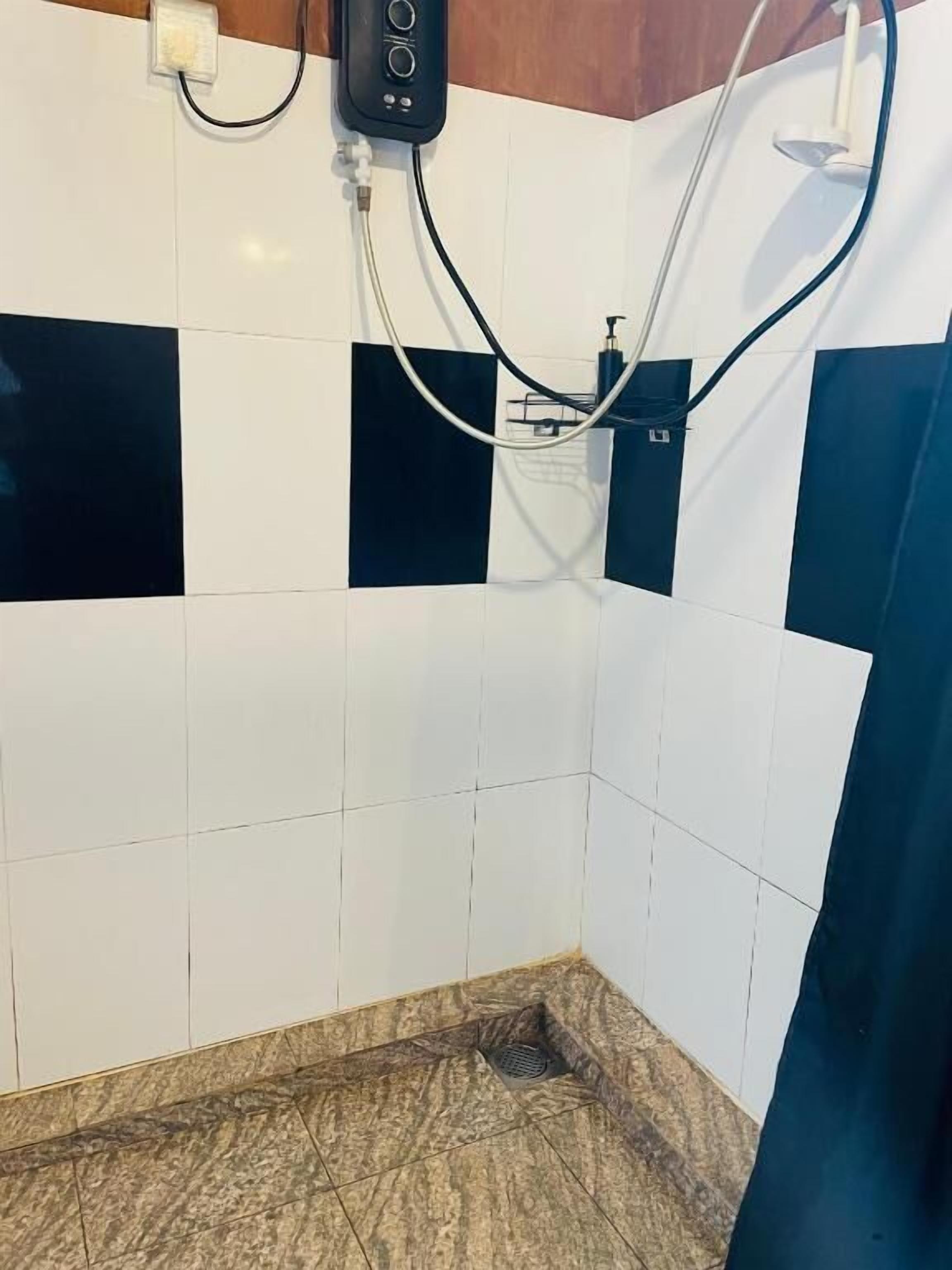 Un baño con azulejos blancos y azul oscuro, una ducha con cabezal de ducha de mano y un desagüe.