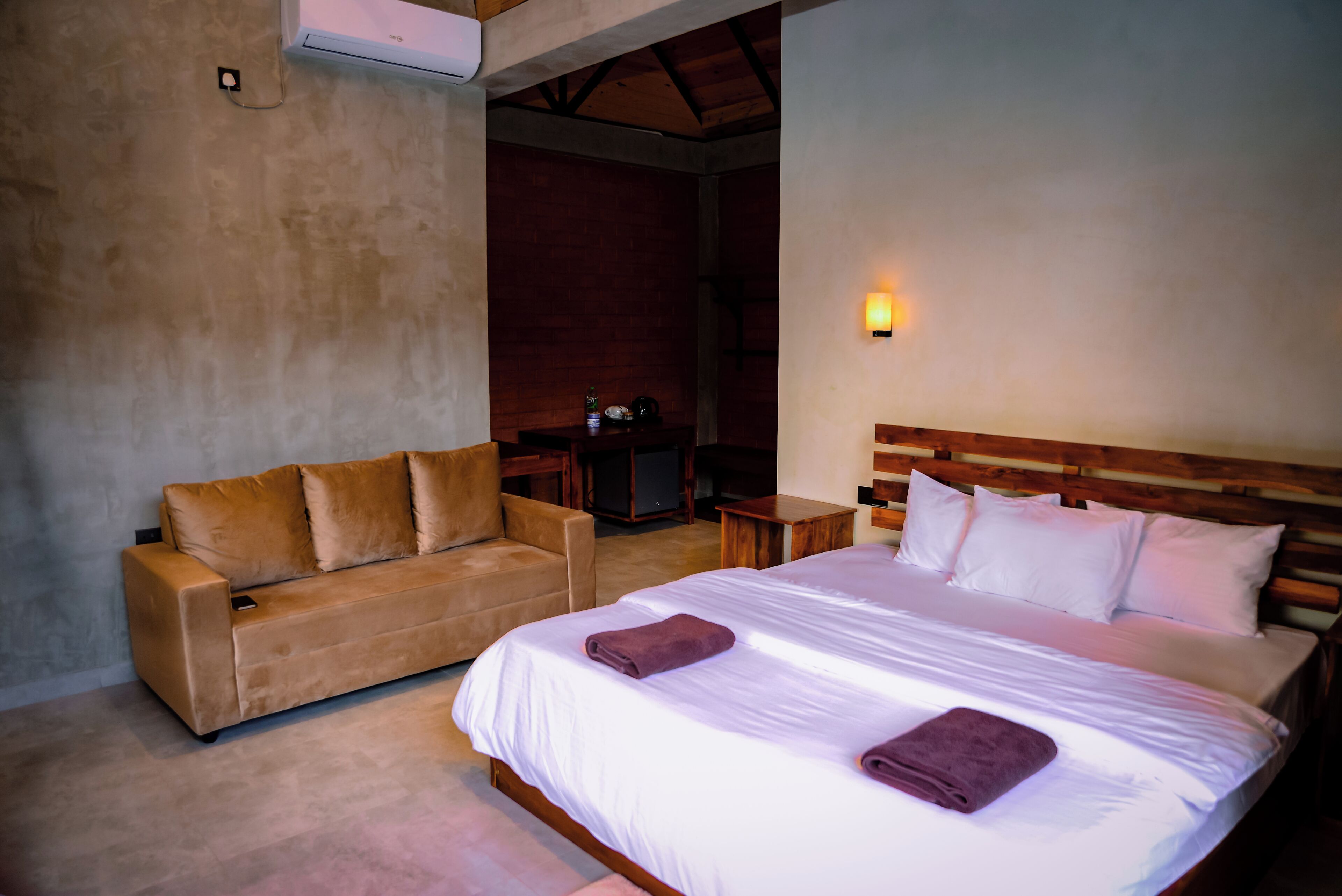 Quarto com cama, sofá, mesa de cabeceira e luminária na parede.