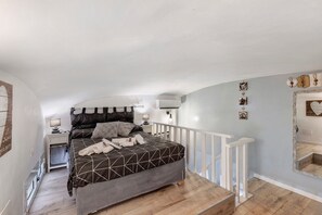 Ein Schlafzimmer mit einem Bett, einem Nachttisch, einer Lampe und einer Treppe, die zu einer oberen Ebene führt.