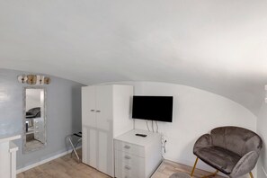 A modern bedroom with a TV mounted on the wall, a wardrobe, a vanity with a mirror, and a plush armchair. - ‘Ludo Home - Rome’ Apartment with Wi-Fi and Air Conditioning (Rome)
