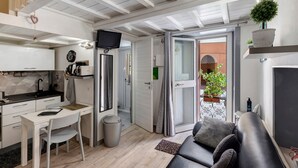 Een knus woongedeelte met een kitchenette, een eethoek, een zithoek met een bank en een klein balkon met potplanten.