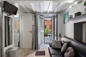 A modern living room with a leather sofa, a flat-screen TV mounted on the wall, and a sliding glass door leading to a balcony. - ‘Ludo Home - Rome’ Apartment with Wi-Fi and Air Conditioning (Rome)