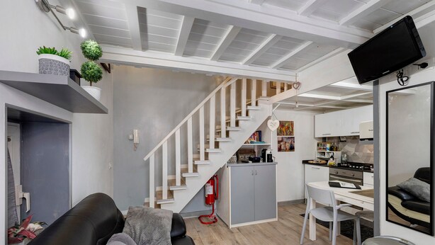 Een modern interieur met een trap, een keukenhoek en een zithoek met een bank en een stoel.
