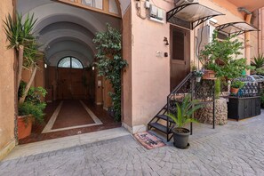 A building entrance with a tiled pathway leading to a door, surrounded by potted plants and a small staircase. - ‘Ludo Home - Rome’ Apartment with Wi-Fi and Air Conditioning (Rome)