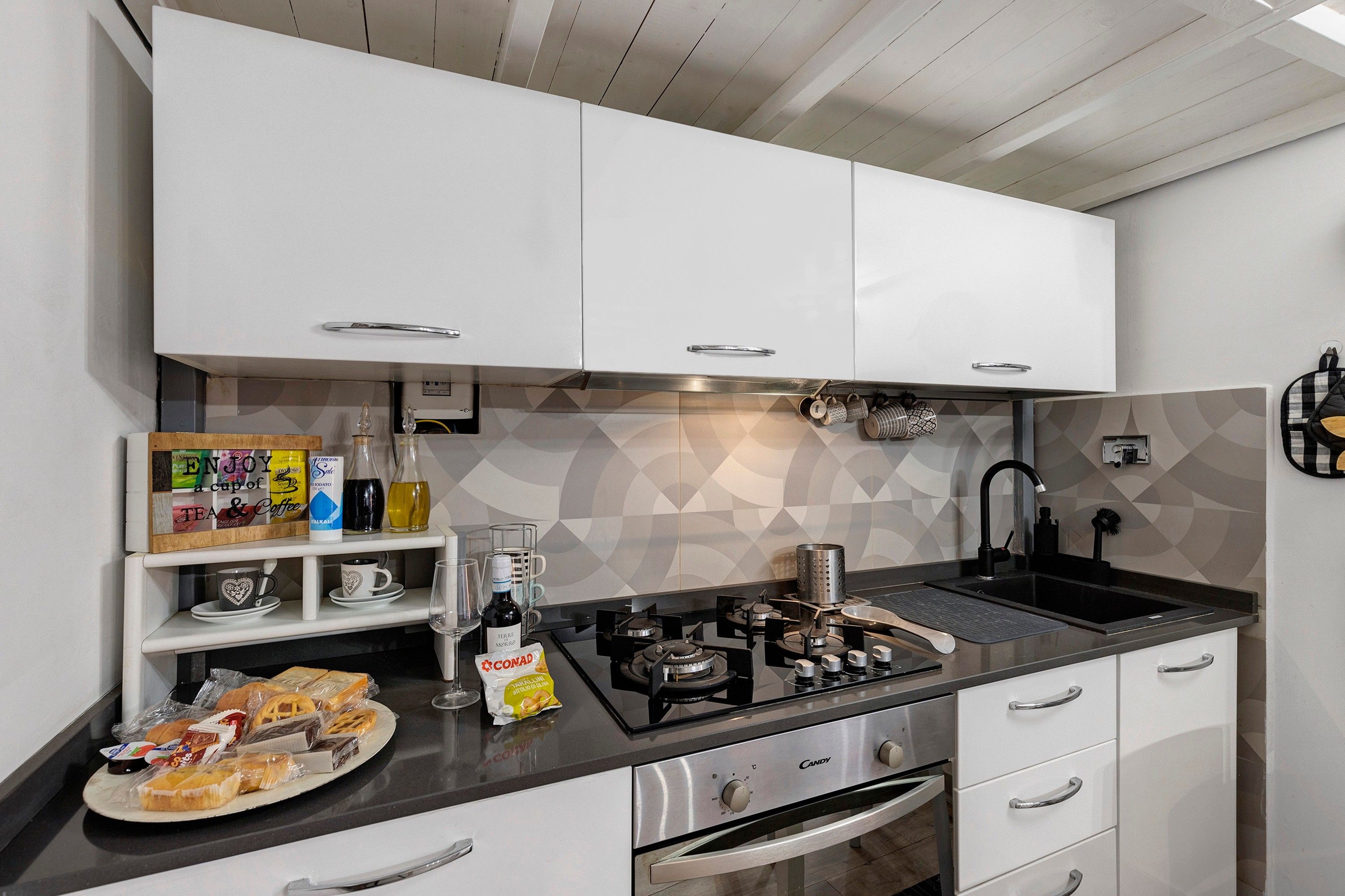 A modern kitchen with white cabinets, a black countertop, and a geometric backsplash.