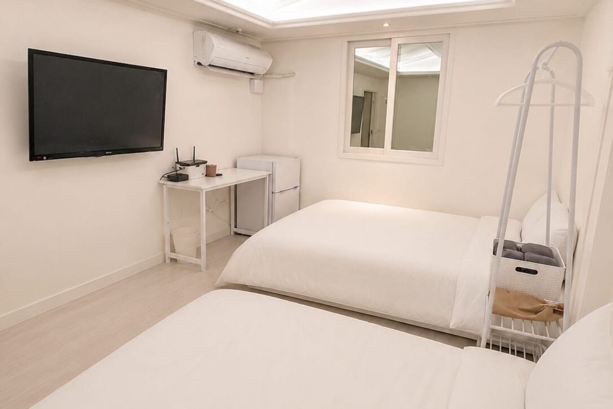 Un dormitorio con televisión de pantalla plana, escritorio, silla, cama y ventana.