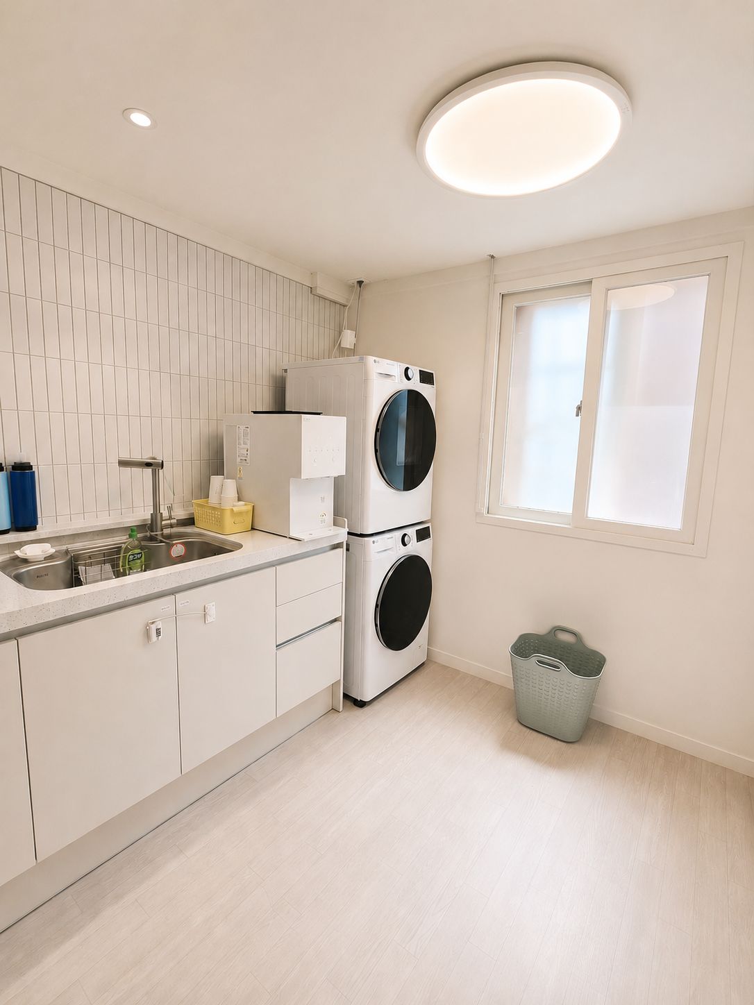 A modern kitchen with a built-in washer and dryer, a sink, and a window with blinds.