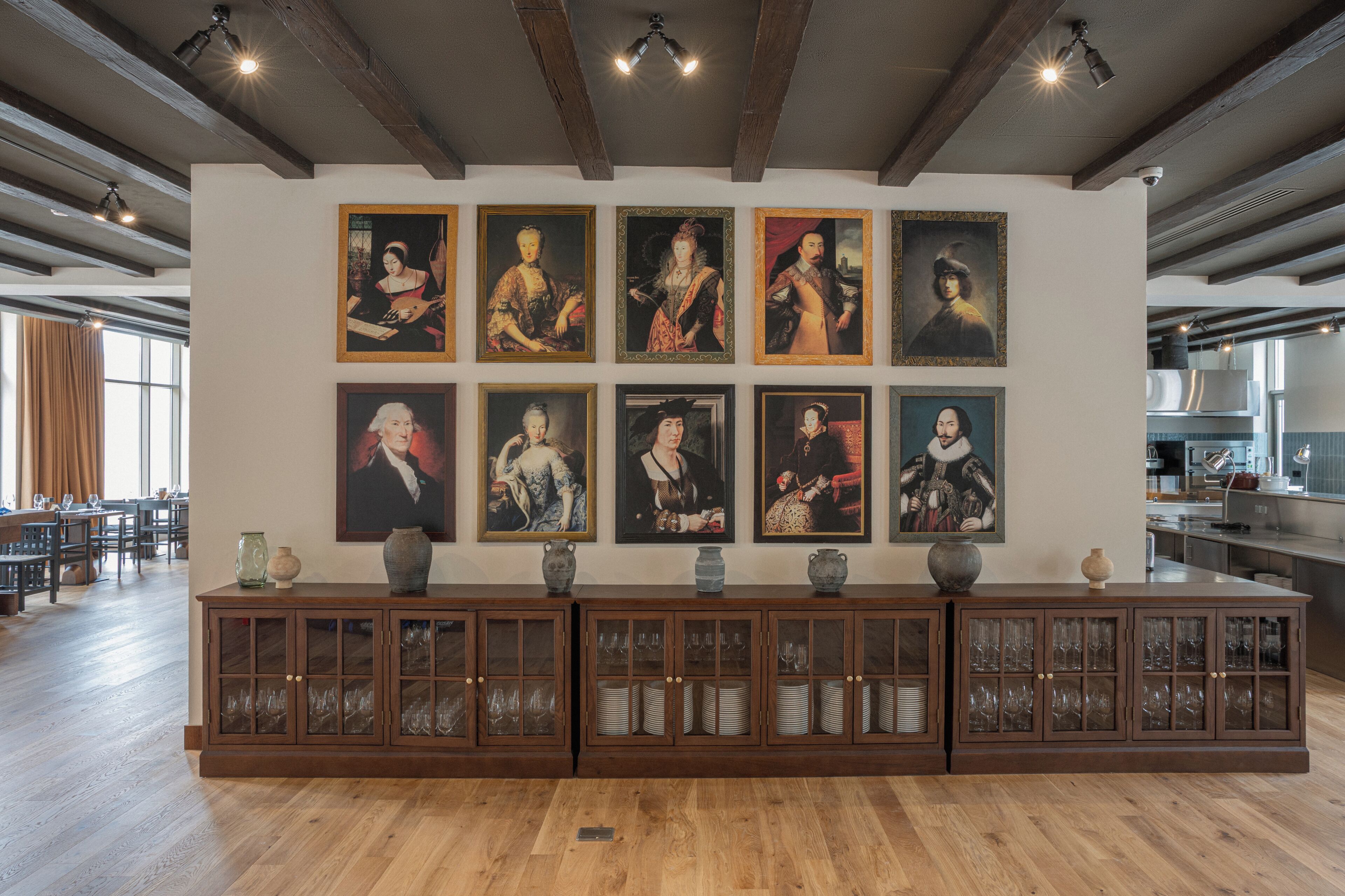 Una pared de galería con retratos enmarcados y un aparador con cristalería.