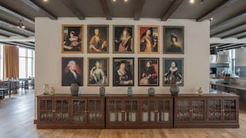 Una pared de galería con retratos enmarcados y un aparador con cristalería.