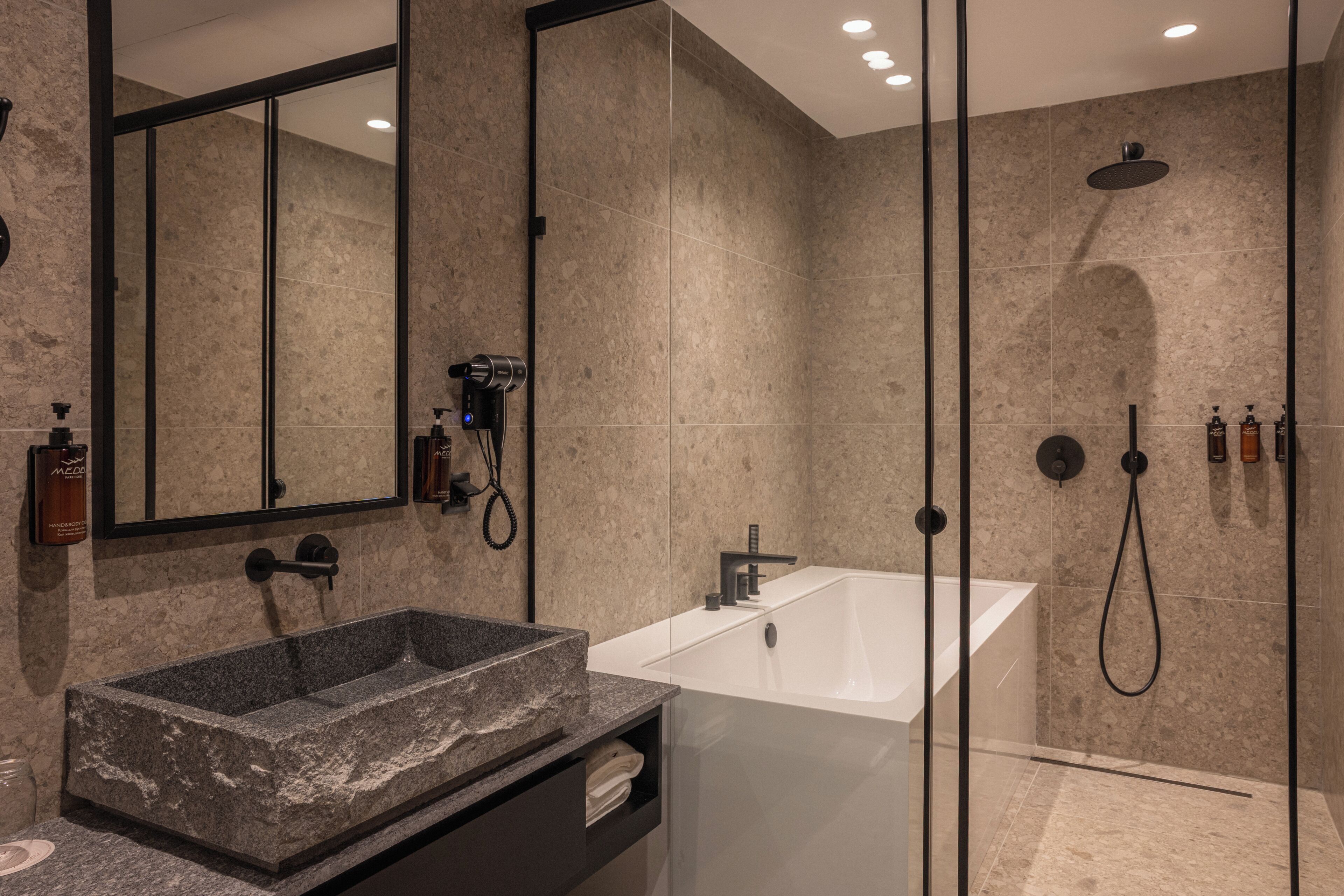 A modern bathroom with a granite sink, a large mirror, a walk-in shower, and a white bathtub.