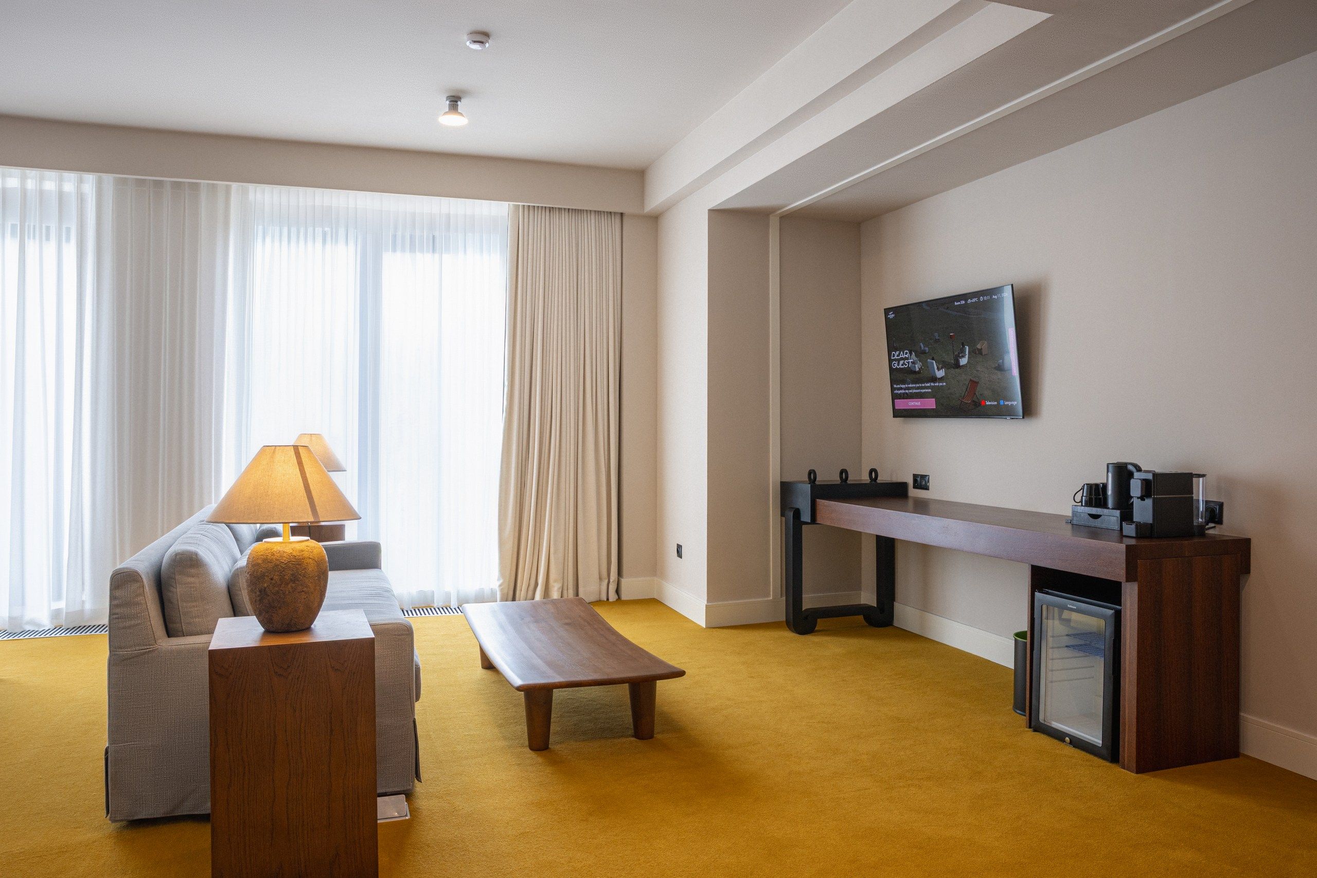 Ein Hotelzimmer mit einer Couch, einem Couchtisch, einem Schreibtisch mit Computer und einem an der Wand befestigten Fernseher.