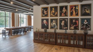 Een eetgedeelte met een lange houten tafel, stoelen en een wand versierd met ingelijste portretten.