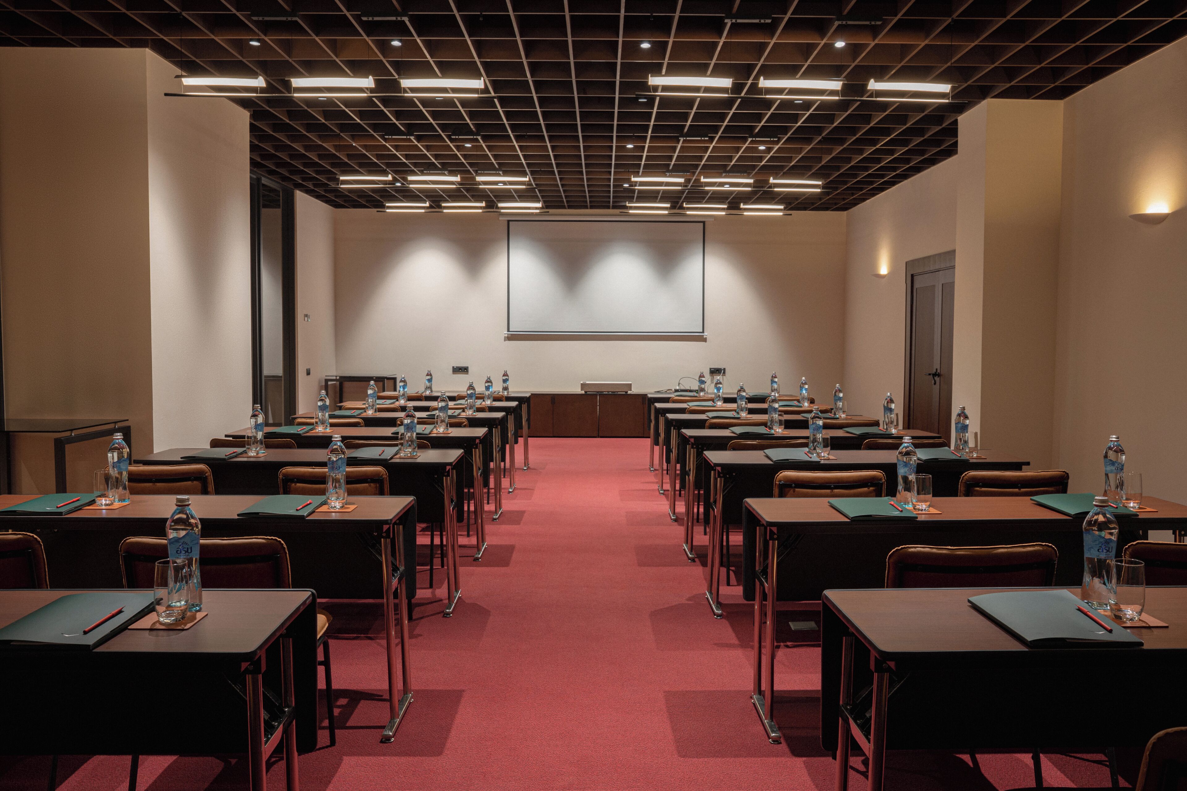 A conference room with rows of tables, chairs, and a projector screen.