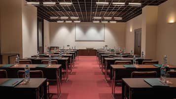 A conference room with rows of tables, chairs, and a projector screen.