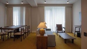 Een hotelkamer met een eettafel, stoelen, een bank, een lamp en een lange bank.