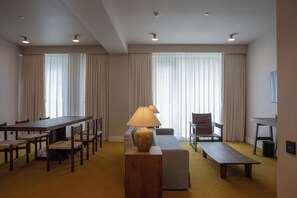 Habitación de hotel con mesa de comedor, sillas, sofá, lámpara y banqueta.