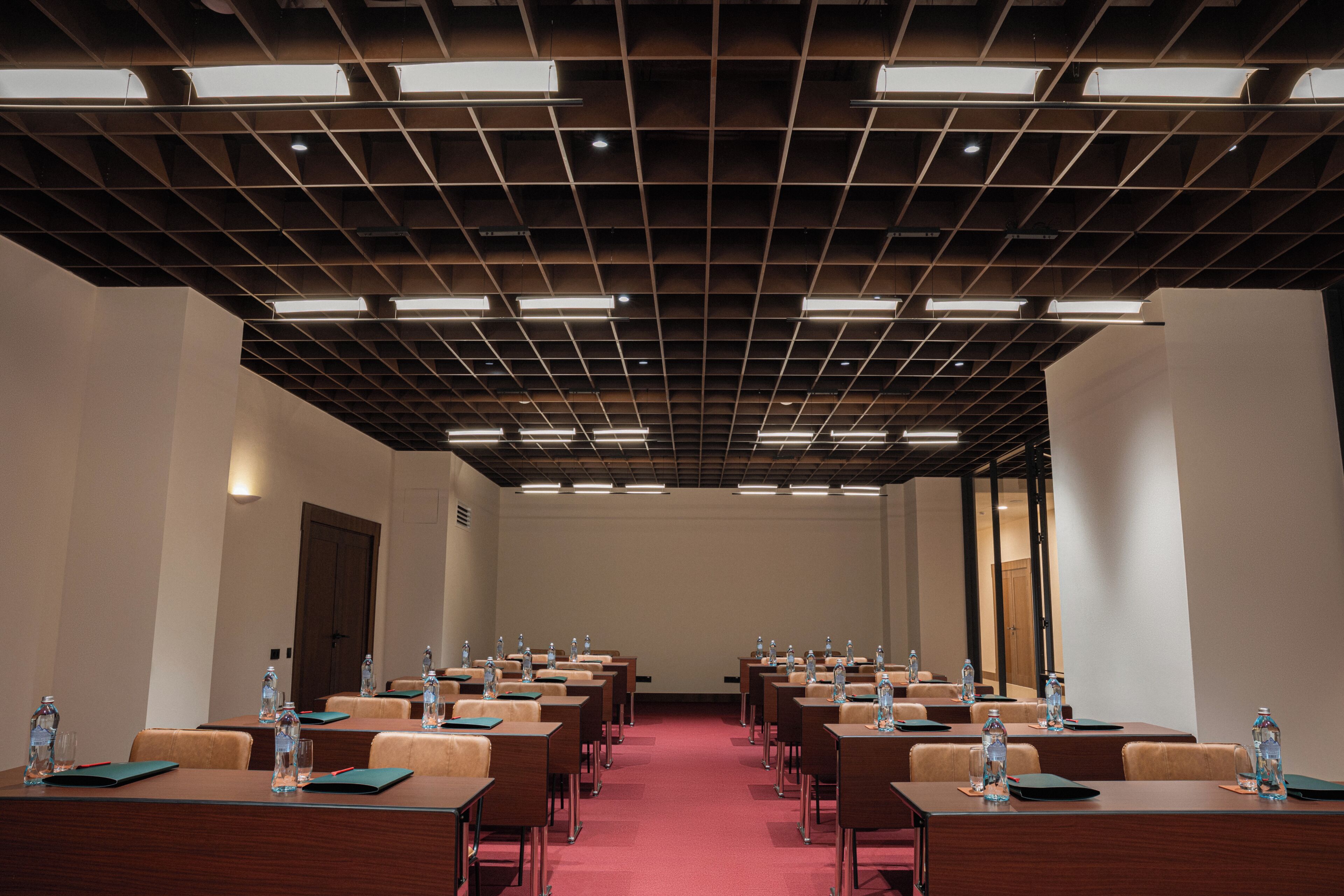 Un salón de conferencias con filas de mesas, sillas y botellas de agua.